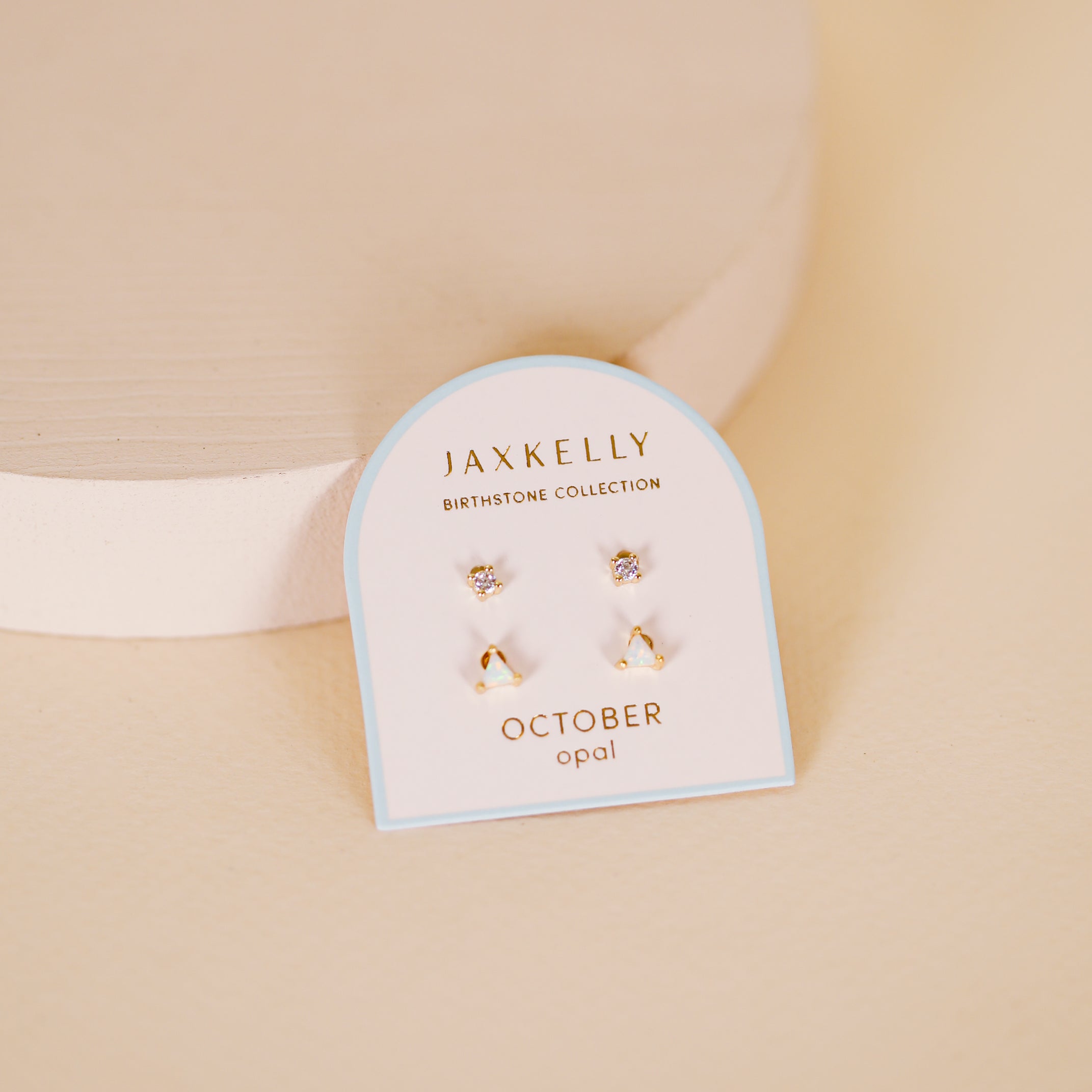 The Birthstone Stud Earring Set - October features opal and gold-plated earrings from the JaxKelly collection, shown on a white card labeled "October opal" with a soft beige background.