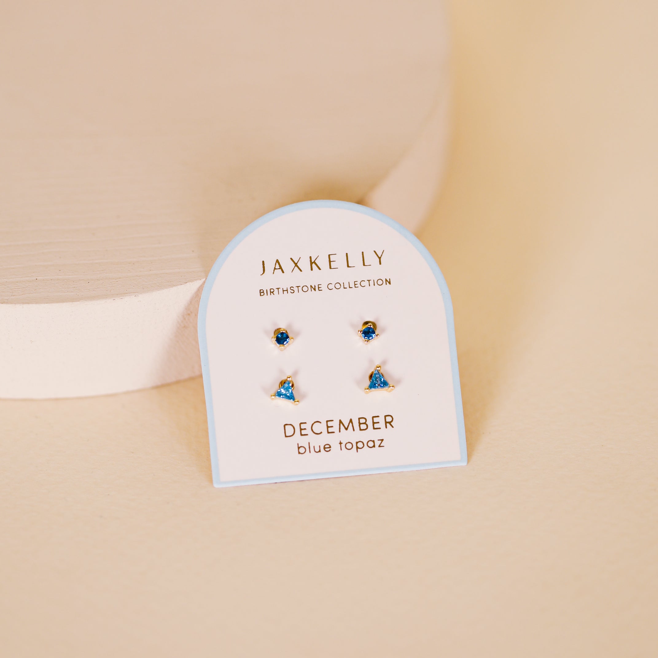 The Birthstone Stud Earring Set - December features blue topaz studs with sterling silver posts, displayed on a JaxKelly Birthstone Collection card labeled December blue topaz against a beige background.