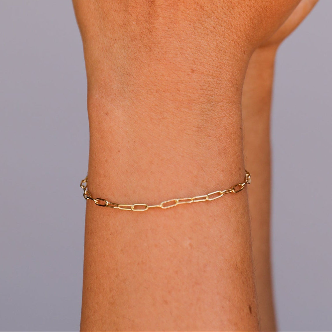 A hand with brown painted nails is shown against a neutral background, adorned with three gold rings and the elegant Small Link Chain Bracelet on the wrist.