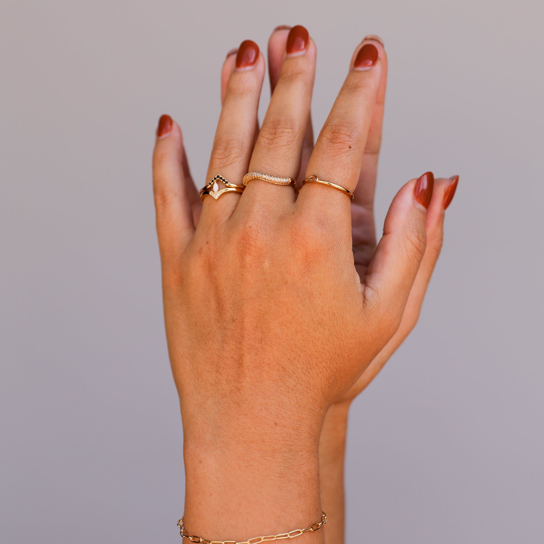 A hand with brown painted nails is shown against a neutral background, adorned with three gold rings and the elegant Small Link Chain Bracelet on the wrist.