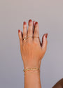 A hand with brown nail polish is shown against a plain background, wearing delicate gold rings and two 18k gold plated adjustable bracelets, including the Chunky Multi Link Chain Bracelet, on the wrist.