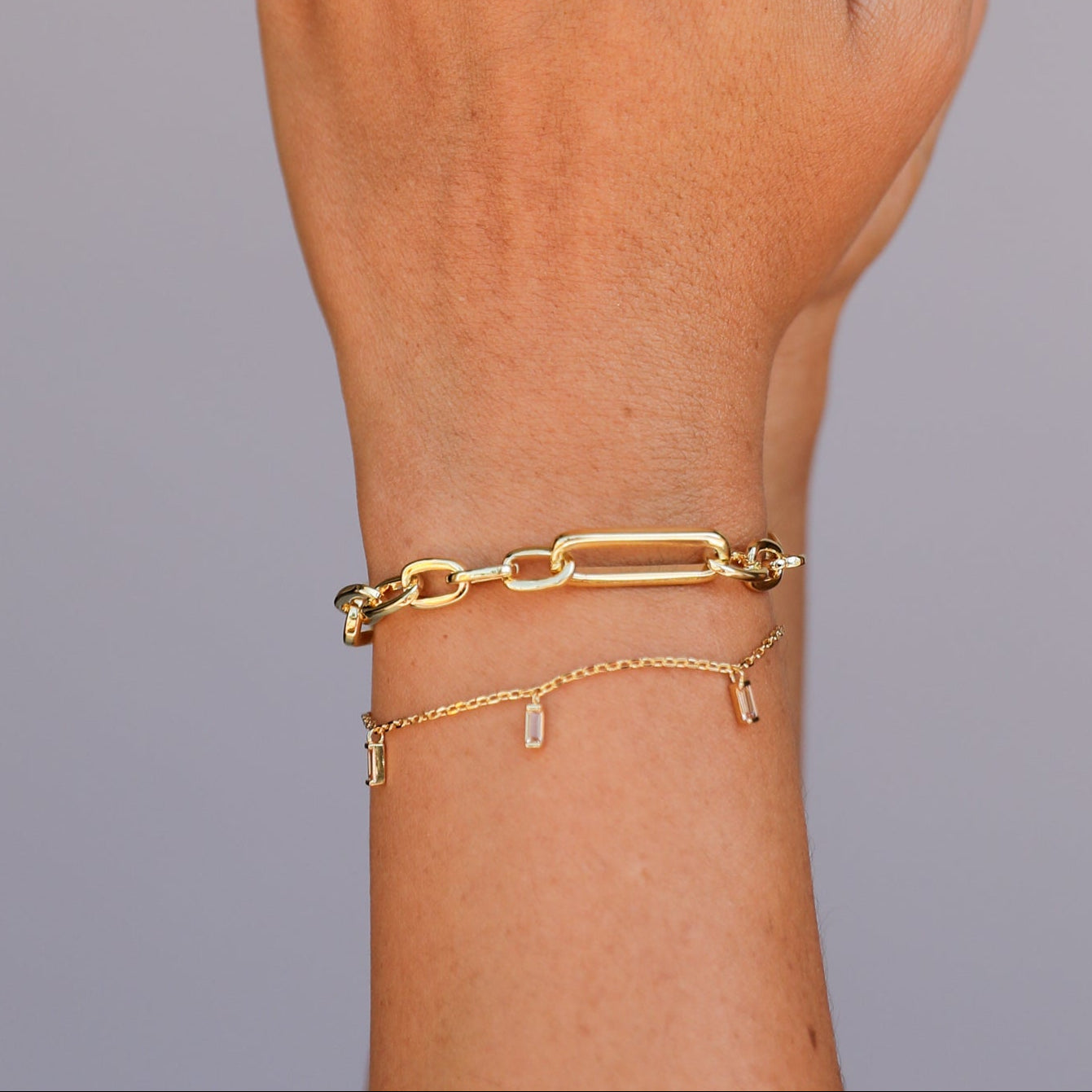 A hand with brown nail polish is shown against a plain background, wearing delicate gold rings and two 18k gold plated adjustable bracelets, including the Chunky Multi Link Chain Bracelet, on the wrist.