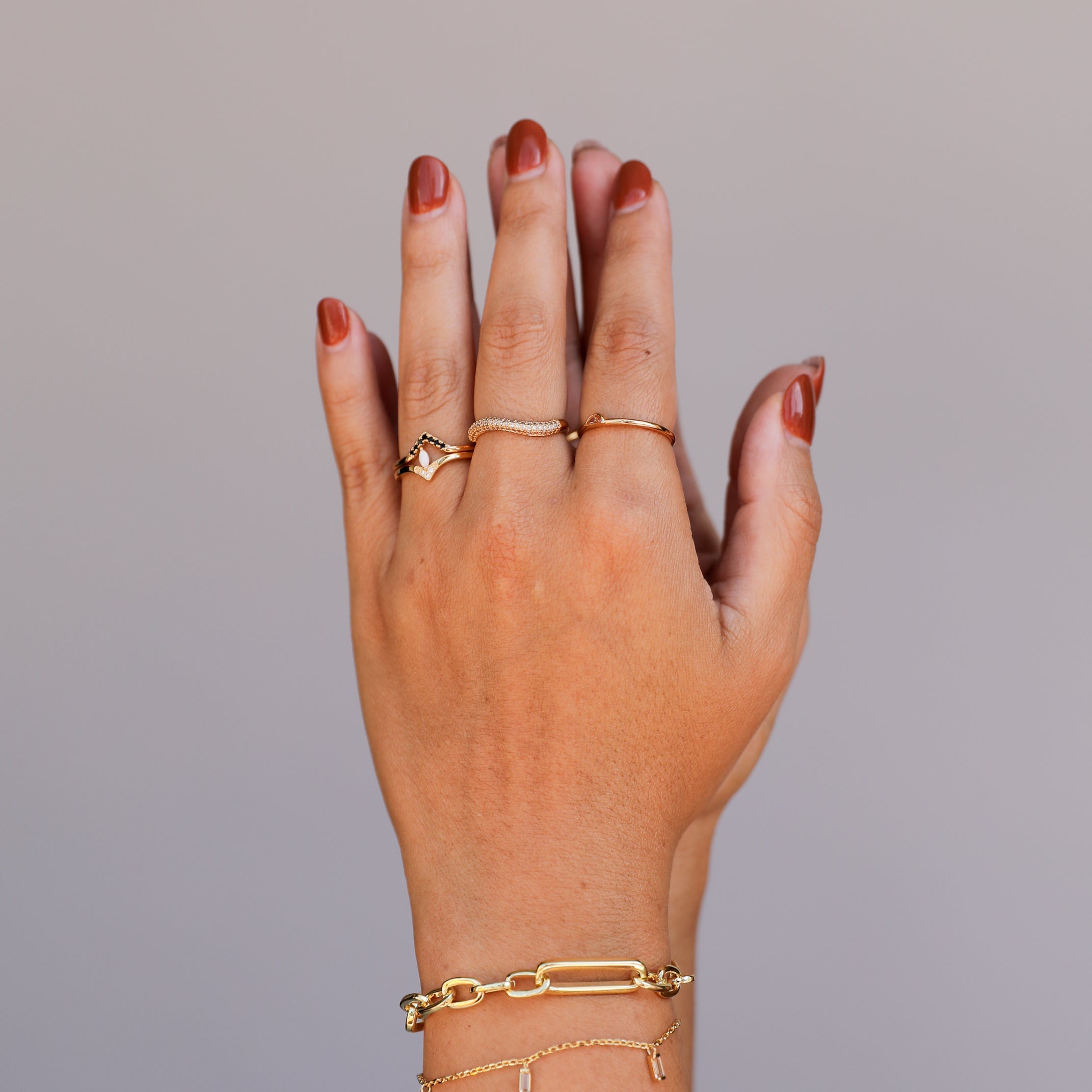 A hand with brown nail polish is shown against a plain background, wearing delicate gold rings and two 18k gold plated adjustable bracelets, including the Chunky Multi Link Chain Bracelet, on the wrist.