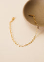The Small Link Chain Bracelet, featuring delicate 18k gold-plated elongated links, is partially placed inside a round beige ceramic dish on a light textured surface.