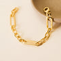 The Chunky Multi Link Chain Bracelet, featuring large rectangular links and plated in 18k gold, is displayed next to a round beige ceramic dish on a light textured surface.