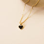 The Gemstone Heart Pendant Necklace - Black Tourmaline, featuring an 18k gold plated chain and a small heart-shaped pendant, is displayed on a textured beige surface beside a round ceramic dish.
