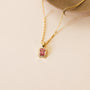 The Rectangular Baguette Pendant Necklace - Light Pink, a delicate 18k gold plated piece with a pink baguette stone pendant, is shown on a beige surface next to a round tan ceramic dish.