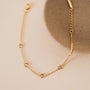 The Champagne Gemstone Bracelet features a delicate gold-plated chain with small round champagne stones, shown beside a round textured beige dish on a light cream background.