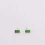 The JaxKelly Emerald Baguette earrings feature gold plated studs with rectangular green gemstones in four-prong settings and sterling silver posts, shown on a plain white background.