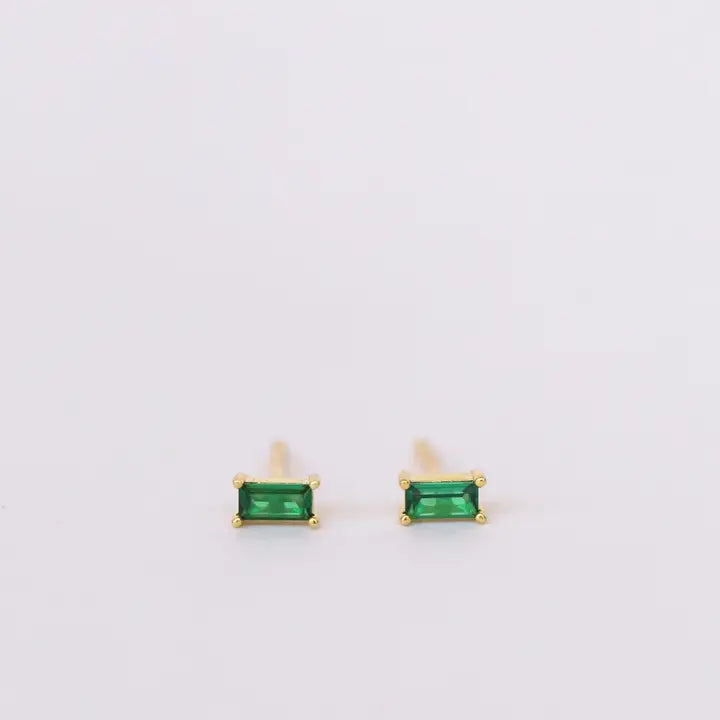 The JaxKelly Emerald Baguette earrings feature gold plated studs with rectangular green gemstones in four-prong settings and sterling silver posts, shown on a plain white background.