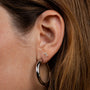 Close-up of an ear adorned with JaxKelly's Double Stud Stack: a small geometric stud in the upper lobe and a thick metallic hoop in the lower lobe. Light brown hair is tucked behind the ear, highlighting each earring’s shine.