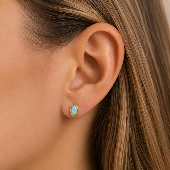 JaxKelly Oval Bezel - Fire Opal stud earrings in an oval-shaped gold bezel setting worn in an earlobe.