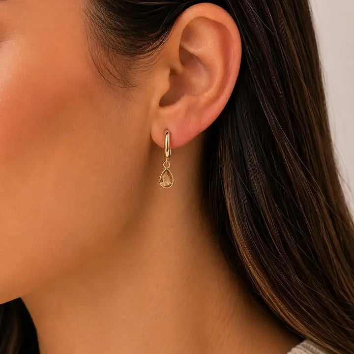 A JaxKelly Teardrop Charm Hoop - Champagne CZ worn on an earlobe, designed as tarnish-free jewelry.