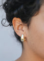 Close-up of a person with curly dark hair wearing the Bold Drop Earring—shiny, gold plated statement hoops with sterling silver posts—against a softly blurred background.