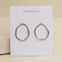The Silver Organic Hoop by JaxKelly, crafted from sterling silver, is displayed on a white card with gold JaxKelly branding, set against a soft beige background.