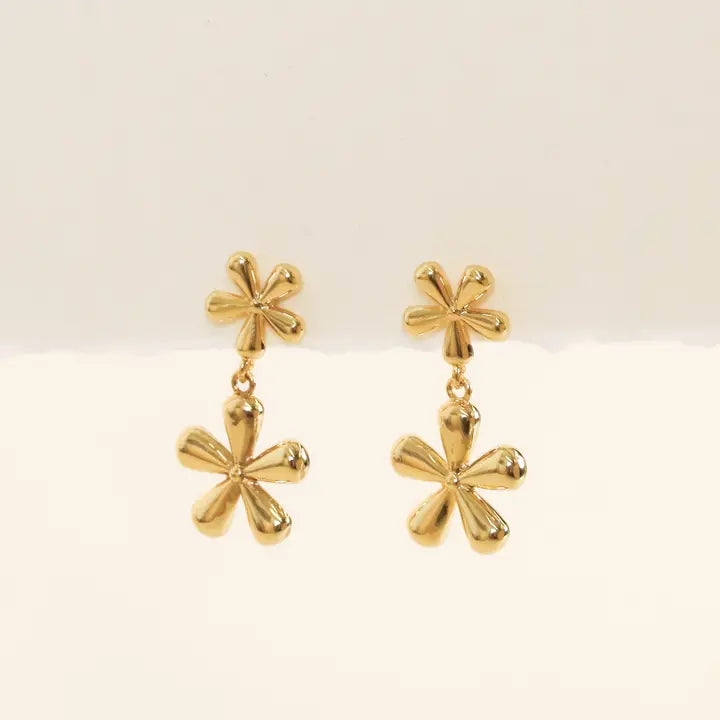 The JaxKelly Double Daisy Drop Earring features two gold-plated sterling silver floral elements—a small daisy on top and a larger, shiny daisy below—displayed against a plain light background.