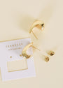 The Bold Drop Earring, featuring gold-plated hoops with sterling silver posts, is shown on a cream surface beside a white JaxKelly “Wear Good Vibes” card, with earring backs placed nearby.
