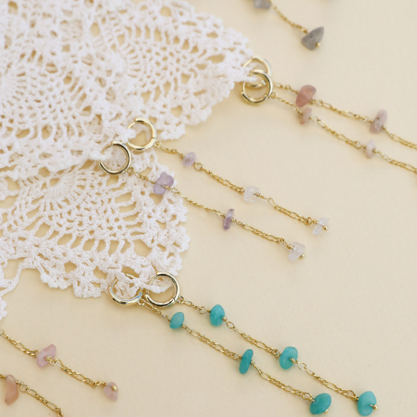 Gold beaded drop earrings with colorful gemstones on lace background