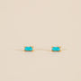 The Turquoise Baguette features small rectangular turquoise stud earrings set in gold with sterling silver posts, shown on a plain beige background.