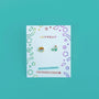 Bookworm Enamel Flat Back Kids Earrings—colorful, hypoallergenic studs for sensitive ears, shaped like a book stack and a globe. Displayed on a white JaxKelly card with playful doodles; features kid-friendly posts.