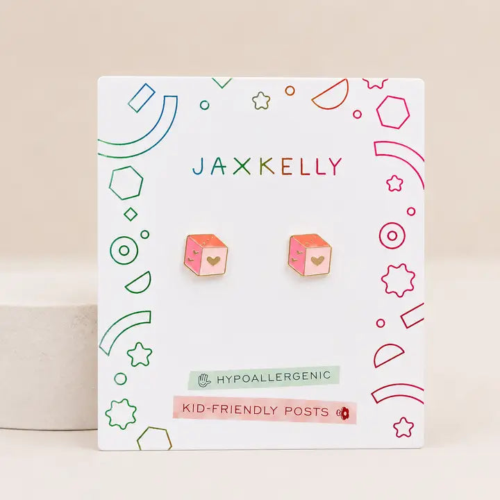 A pair of Pink Dice Enamel Flat Back Kids Earrings by JaxKelly, featuring cube-shaped pink and orange dice with heart details, displayed on a branded card reading “Hypoallergenic and Kid-Friendly Posts” with colorful geometric accents—perfect for sensitive ears.