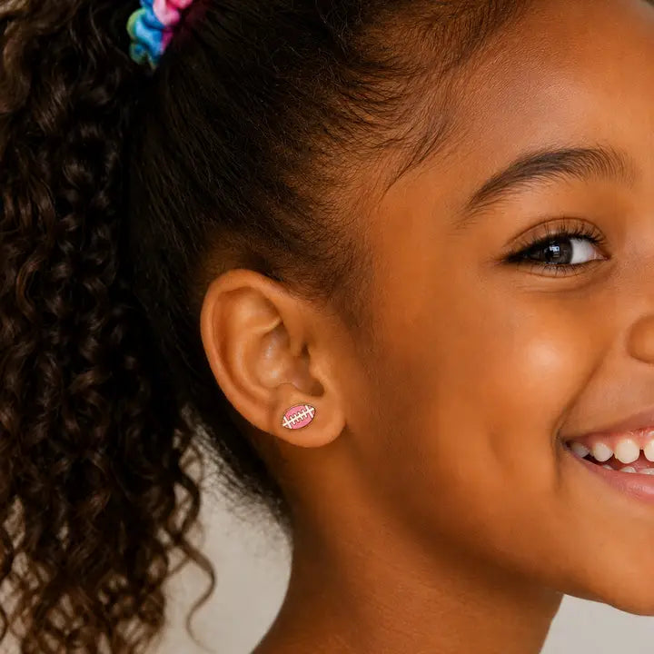 A young girl wearing a pink enamel Football Enamel Flat Back Kids earring.