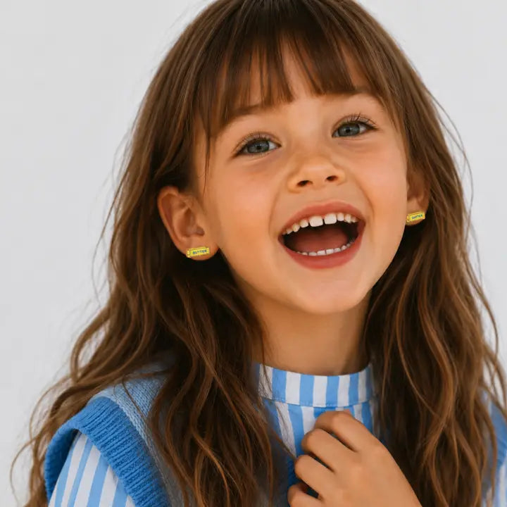 A young girl laughing while wearing small, rectangular, butter-shaped Butter Enamel Flat Back Kids Earrings.