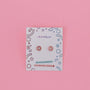 A pair of Donut Enamel Flat Back Kids Earrings with pink hypoallergenic studs and small gems, shown on a playful JaxKelly card with blue and red doodles on a solid pink background. The card highlights that the earrings are kid-friendly.