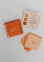 A set of orange and peach waterproof cards from Positivity Shower Affirmations™ is spread out on a white surface, with one card reading “Loving people will enter my life,” accompanied by the branded packaging.