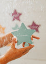A person holds a blue-green star with "I am lovable" from Kids Shower Affirmations™. Water splashes and colorful stars decorate the white background—fun, positive affirmations perfect for children.