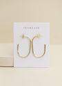 A pair of JaxKelly Gold Large Open Hoop earrings, hypoallergenic and displayed on a white JaxKelly card, set against a neutral beige background.