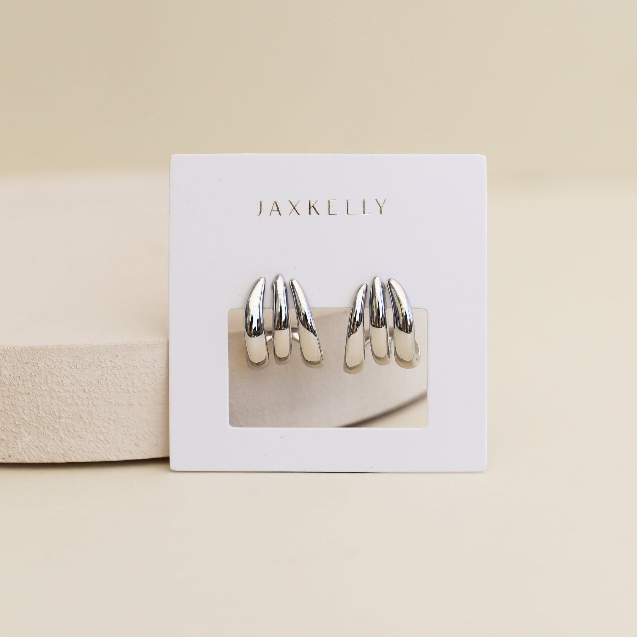 The Silver Three Hoop Huggie earrings feature a modern, layered sterling silver design displayed on a white JaxKelly card—perfect minimalist accessories to elevate any look.
