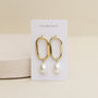 The Oval Pearl Drop earrings feature 18k gold plated elongated hoops with dangling white pearls, showcased on a JaxKelly card against a neutral background.