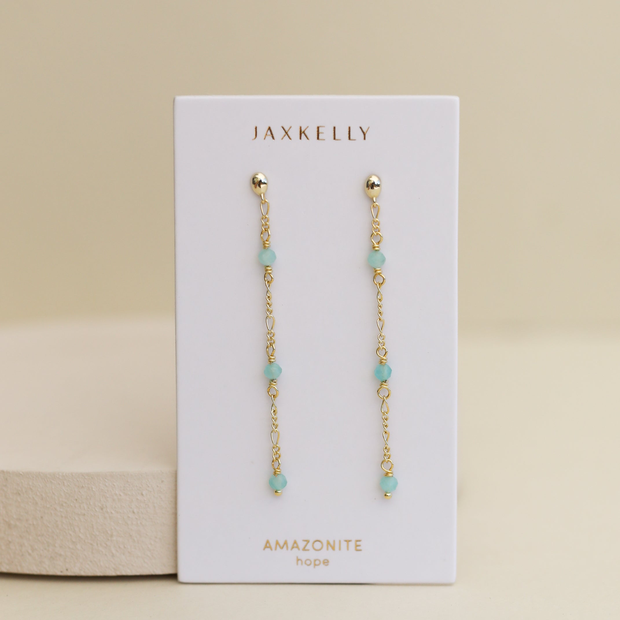 A pair of Gemstone Chain Drop - Turquoise earrings, 18k gold plated with small turquoise beads, displayed on a white JaxKelly card—ideal for lovers of bohemian jewelry.