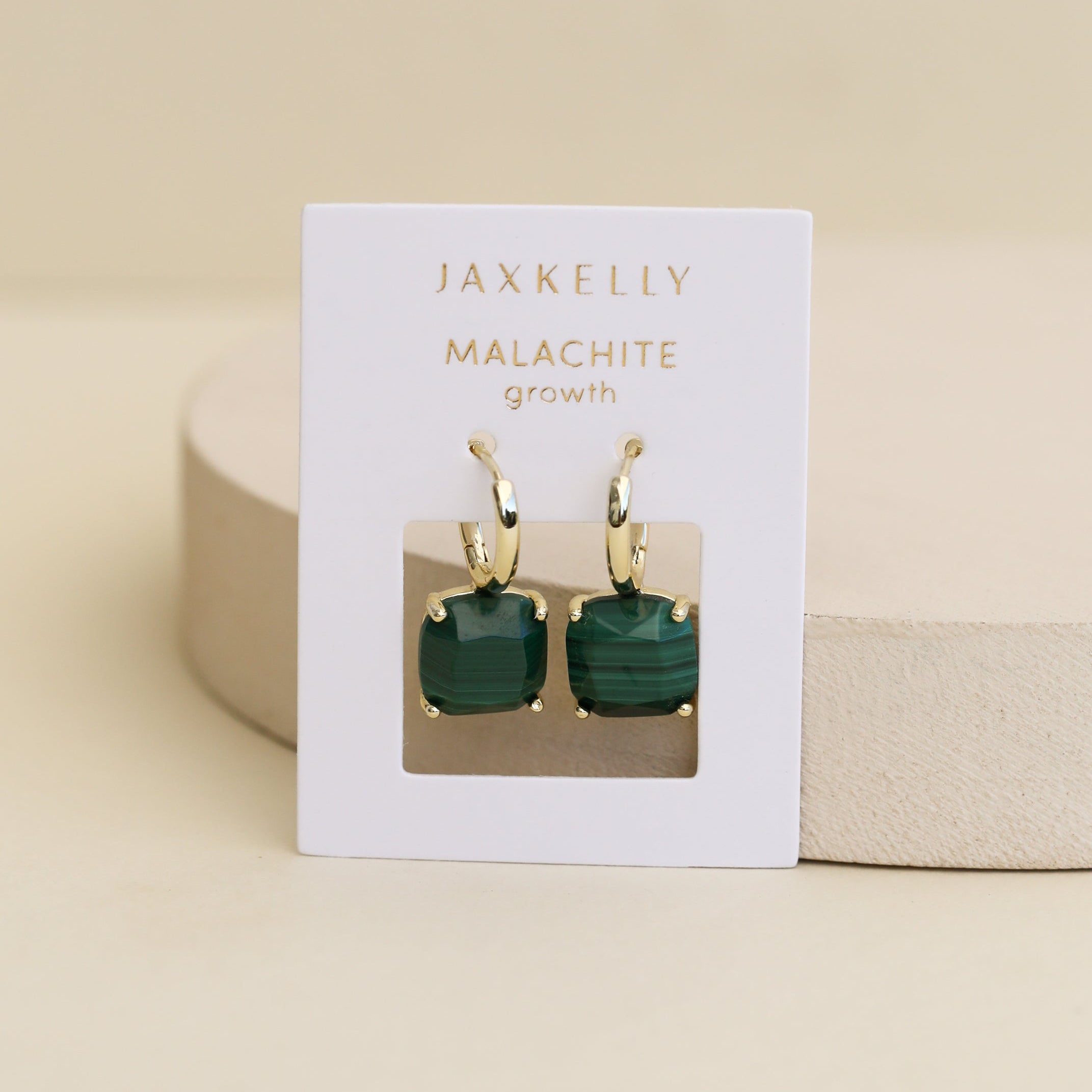 The Gemstone Mini Drop - Malachite earrings feature square green stones with 18k gold plating, displayed on a white JaxKelly card labeled "MALACHITE growth" against a neutral beige background.