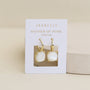 A pair of Gemstone Mini Drop - Mother of Pearl earrings with gold hoops is displayed on a white JaxKelly card, labeled "Mother of Pearl calming," set against a soft beige background.