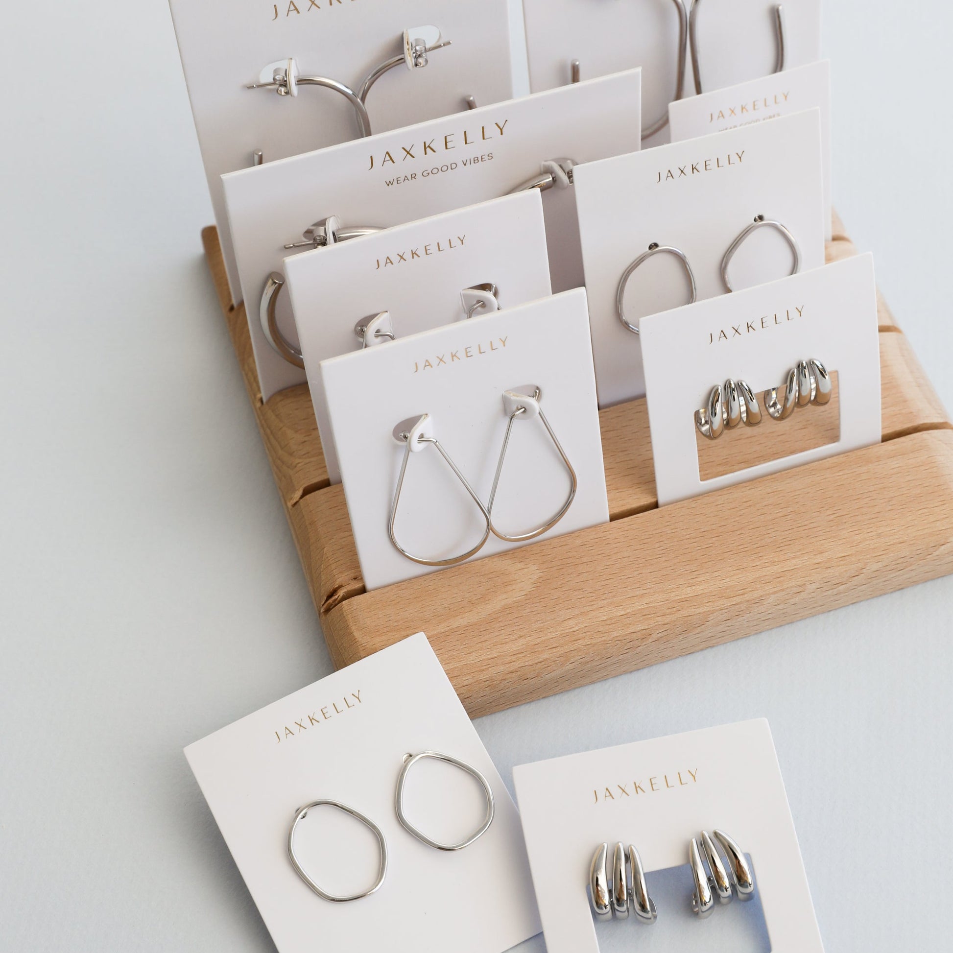 JaxKelly Mystery Earrings are displayed on white cards, neatly arranged on a wooden stand with two extra pairs in front—perfect for fans of surprise jewelry.