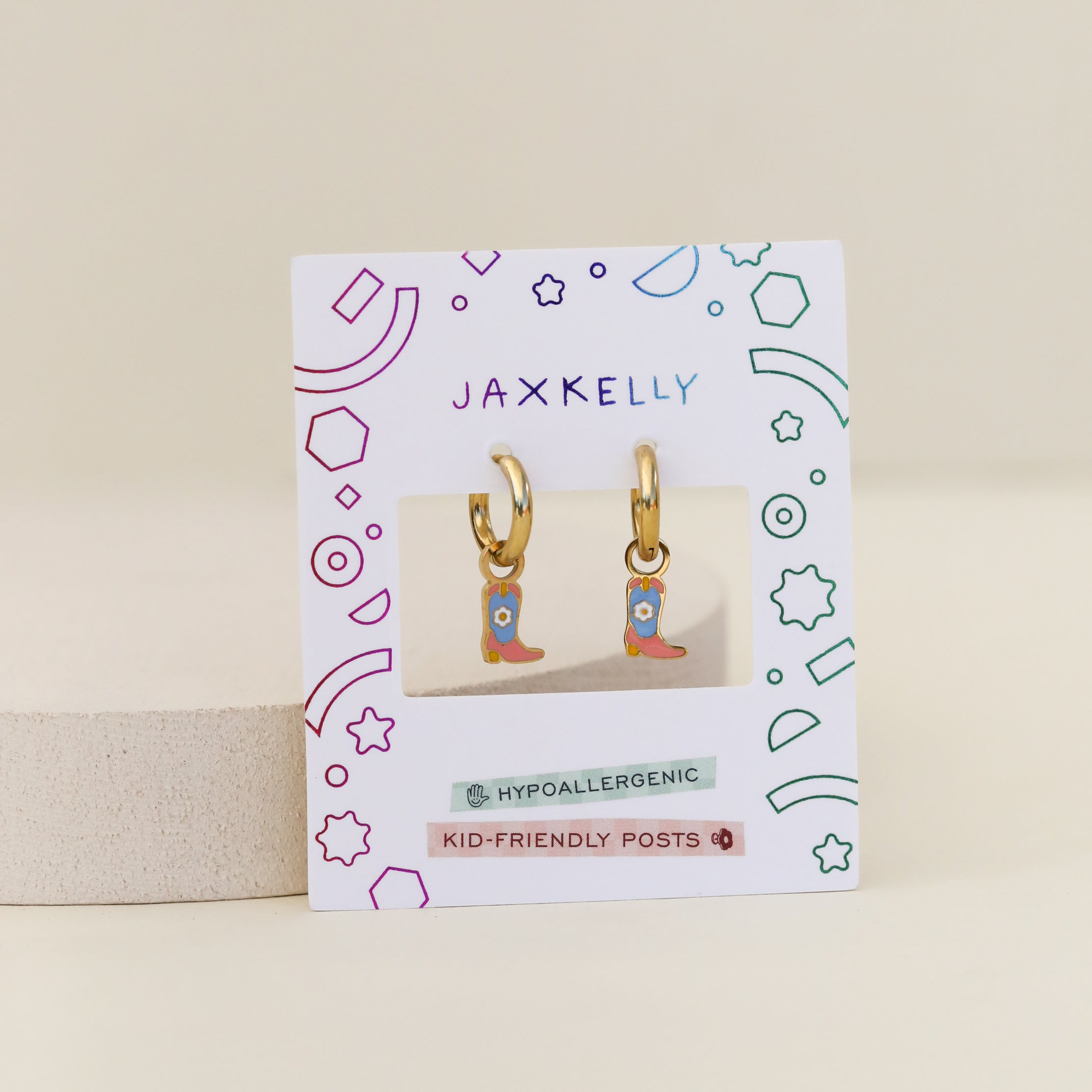 Boot Enamel Charm Hoop earrings feature colorful cowboy boot charms and come on a playful JaxKelly card. Hypoallergenic and kid-friendly, they're perfect for sensitive ears, with fun geometric designs on the packaging.