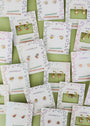 Bow Enamel Charm Hoop earrings for kids, displayed on JaxKelly cards in a playful overlapping arrangement. These hypoallergenic hoops shine on a pale green surface and feature colorful enamel bow designs.
