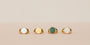 Four Gold Signet Rings are neatly arranged on a light beige surface, each crafted with 18k gold plating and featuring unique round accents in white, gold, green, and white—ideal for effortless everyday wear against a cream background.