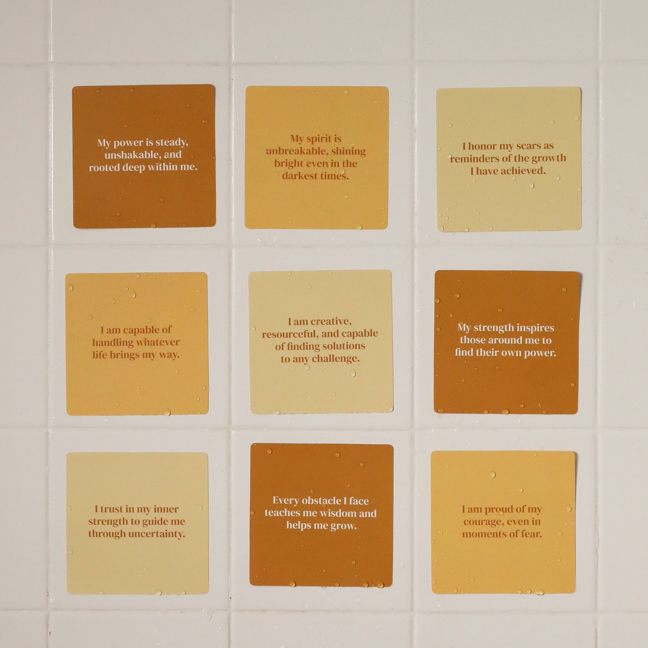 The Strength Shower Affirmations™ set features twelve square tiles in cream, tan, and brown, each with an inspiring message at the center, offering encouragement and empowerment during your daily routine.