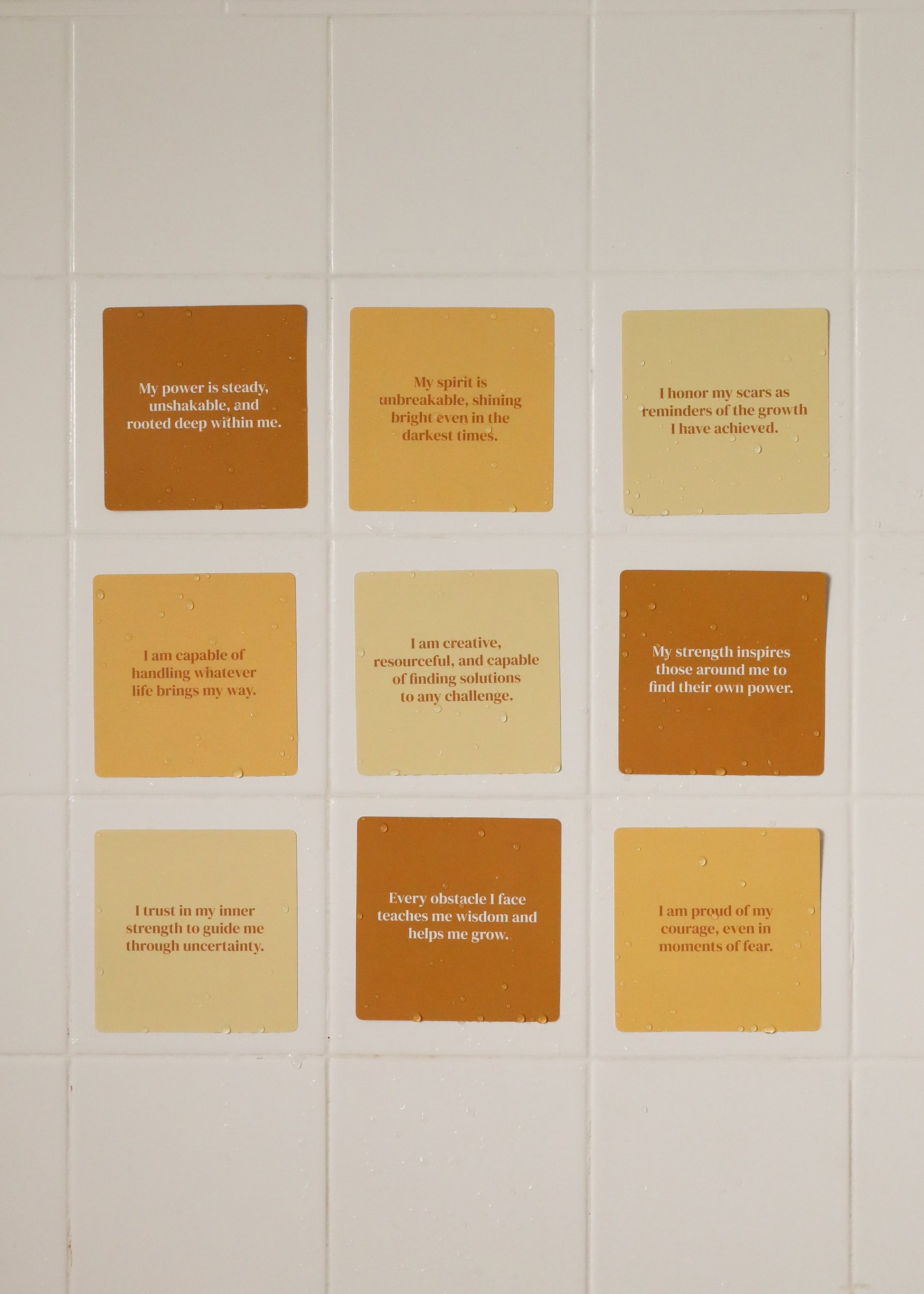 The Strength Shower Affirmations™ set features twelve square tiles in cream, tan, and brown, each with an inspiring message at the center, offering encouragement and empowerment during your daily routine.