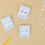 Three Dinosaur Enamel Flat Back Kids Earrings sets are displayed on decorative cards atop a beige surface, surrounded by colorful candies and two striped birthday candles—one yellow, one white with dots. Perfect for sensitive ears.