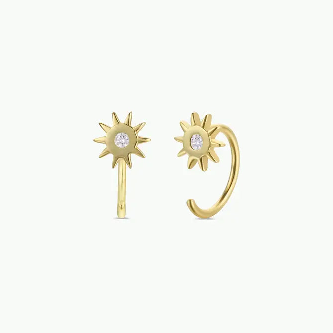 JaxKelly Sun Huggie earrings feature gold-plated sunburst designs with a central sparkling gemstone, shown against a simple light background.