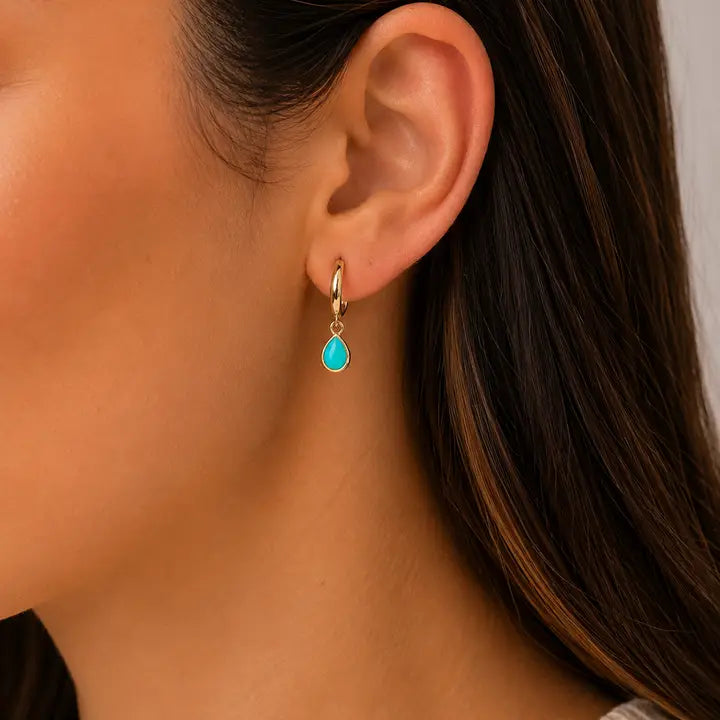 A JaxKelly Teardrop Charm Hoop - Turquoise worn on an earlobe.