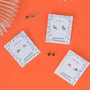 Three pairs of Dinosaur Enamel Flat Back Kids Earrings, ideal for sensitive ears, are shown on illustrated cards with star and rainbow designs against a bright orange background. Extra earrings and a paper decoration accent the corners.