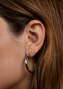 Close-up of a person's ear with timeless jewelry: a small square stud in the upper lobe and Silver Everyday Hoop - Medium in the lower lobe. The person has light brown hair.