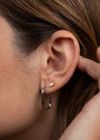 A close-up shows a person's ear with brown hair, wearing the Silver Rectangle Hoop - Large earring: a thick, large sterling silver rectangular hoop. A hand appears near the ear.