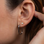 Close-up of a person with light brown hair gently touching their ear, wearing the White Opal Baguette stud earring—featuring a lab-grown white opal—and a larger, U-shaped silver hoop.