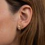 Close-up of a woman's ear with straight, light brown hair wearing two gold earrings: the Sun Ray - White Opal earring featuring a lab-grown White Opal, and a small 18k gold plated hoop.
